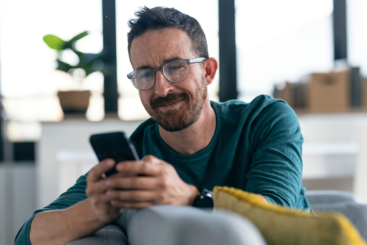 Mann sitzt auf einem Sofa mit einem Handy in der Hand