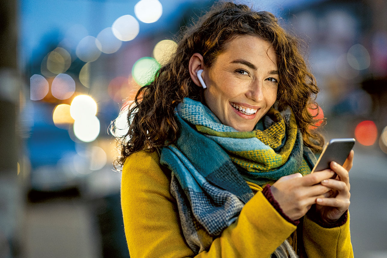 Lächelnde Frau mit Handy in der Hand auf einer Straße