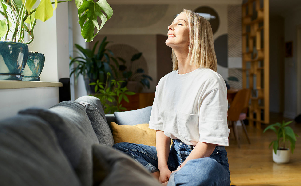Frau sitzt auf einem Sofa und genießt die hereinstrahlende Sonne