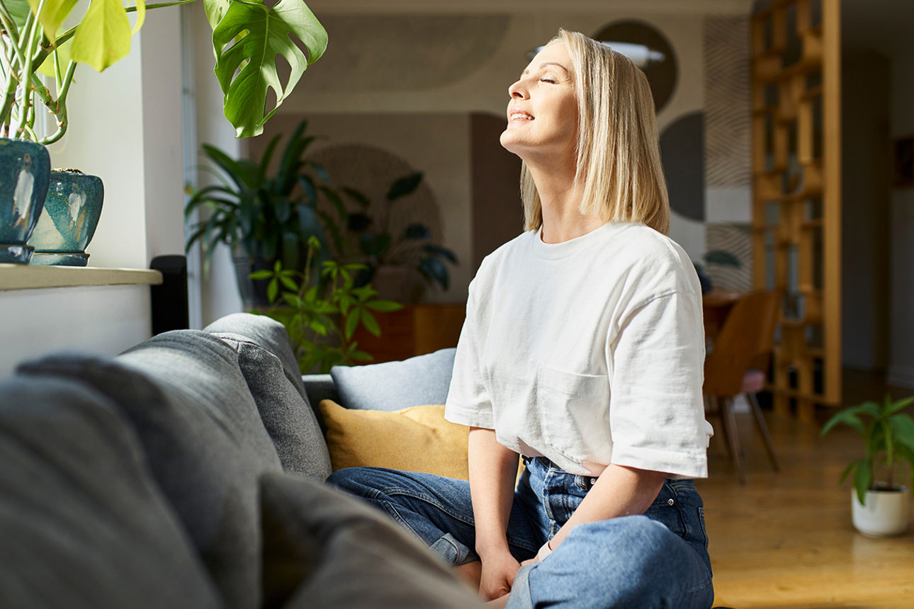 Frau sitzt auf einem Sofa und genießt die hereinstrahlende Sonne