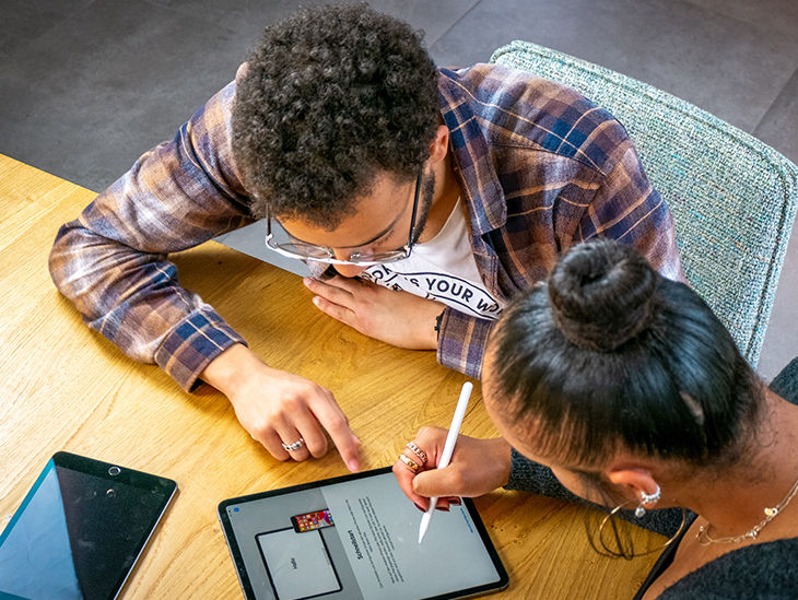 Mann und Frau sitzen zusammen am Tisch und schreiben etwas auf einem Tablet
