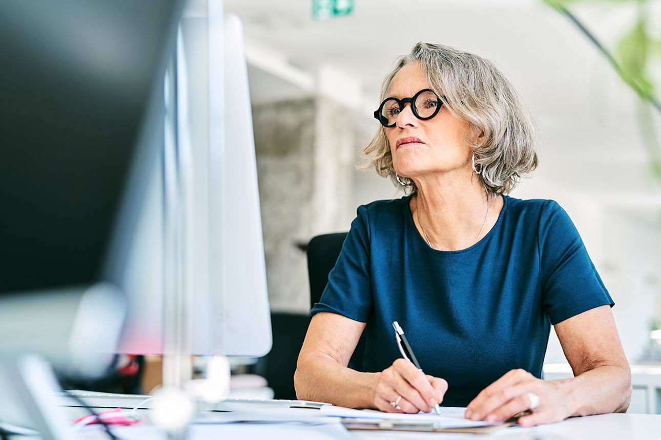 Frau sitzt am Schreibtisch vor einem Computer mit einem Stift in der Hand