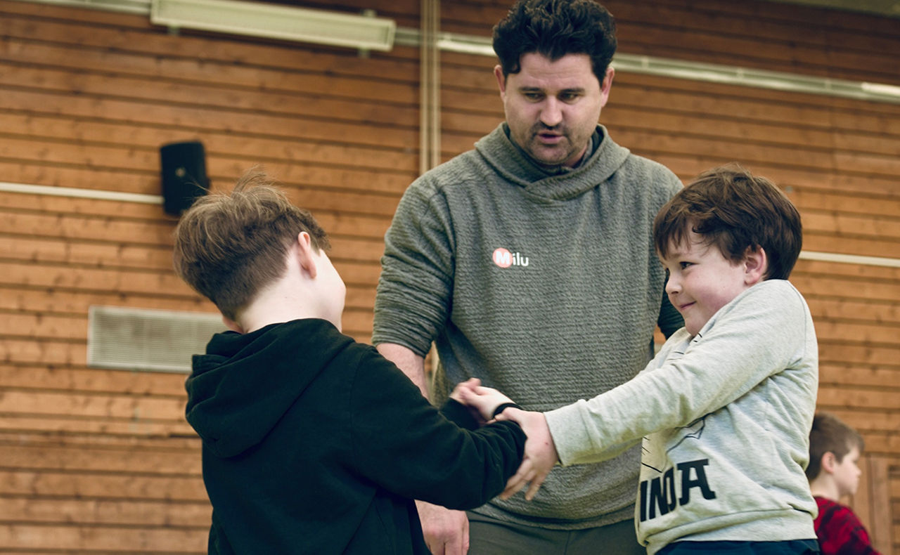 Zwei Kinder kämpfen miteinander und ein Erwachsener beaufsichtigt