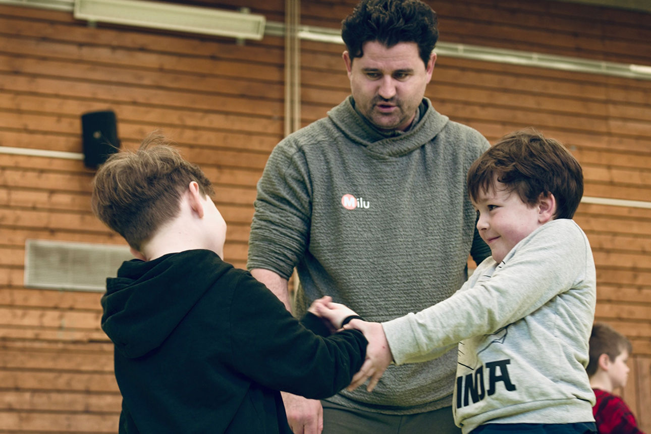 Zwei Kinder kämpfen miteinander und ein Erwachsener beaufsichtigt
