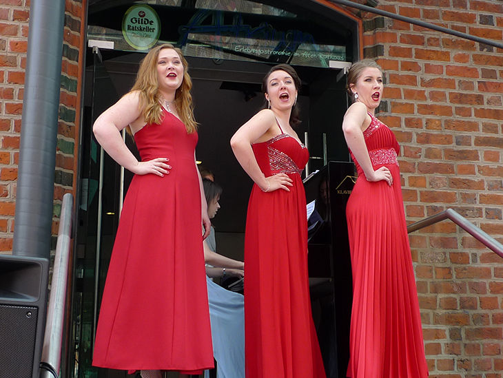 Drei Frauen in roten Kleidern singen