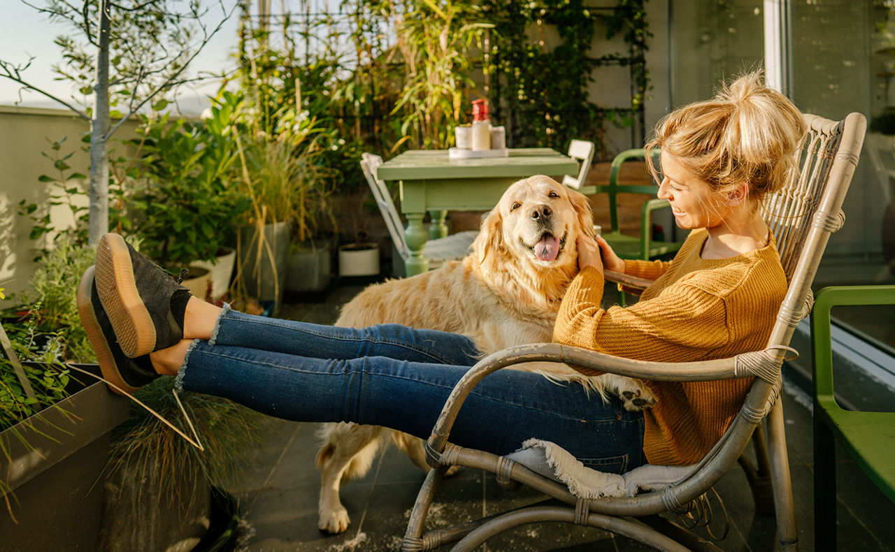 Frau mit Hund auf dem Schoß im Stuhl sitzend af einer Terrasse