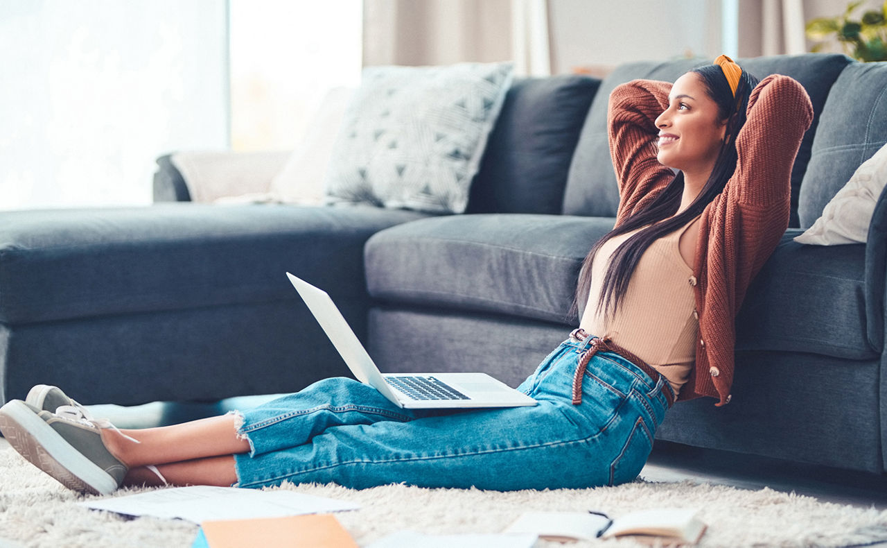 Frau mit Laptop auf dem Schoß sitzt vor einem Sofa