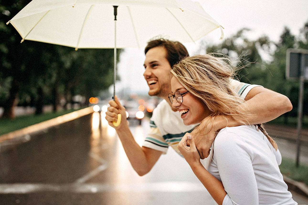 Mann und Frau stehen umarmt zusammen und der Mann hält einen Regenschirm