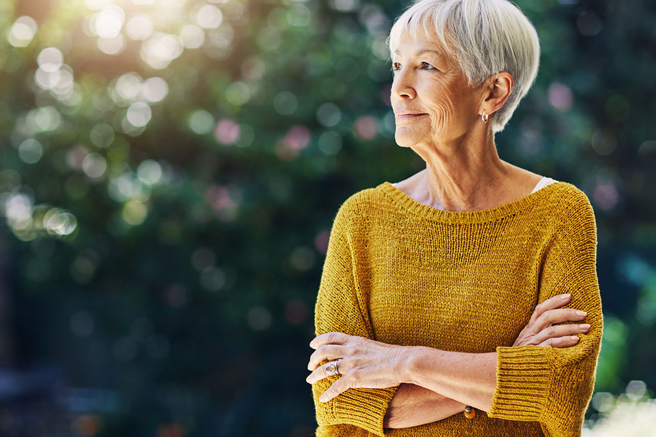 Ältere Frau mit verschränkten Armen guckt in die Ferne
