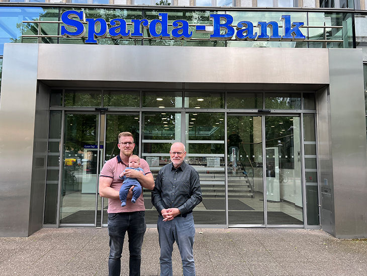 Bild von zwei Männern und einem Baby vor dem Sparda-Bank Gebäude in Hannover
