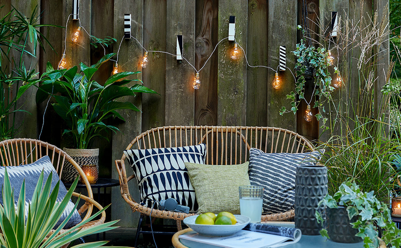 Gartenbank mit Stuhl und Tisch sowie Lichterkette und Pflanzen