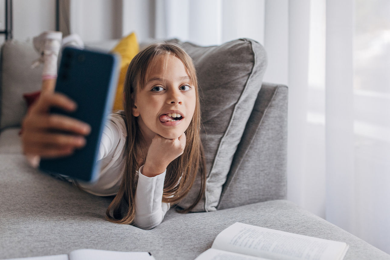 Junges Mädchen liegt auf dem Sofa und macht ein Selfie