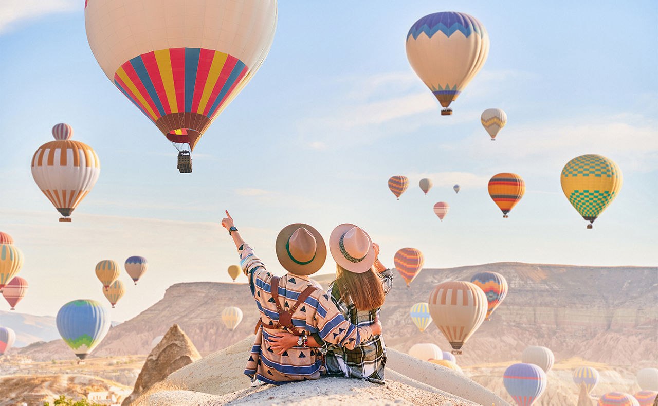Paar sitzt vor einer Landschaft mit mehreren Heißluftballons