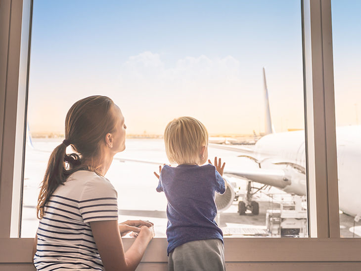 Mutter und Kind beobachten am Fenster die Flugzeuge am Flughafen