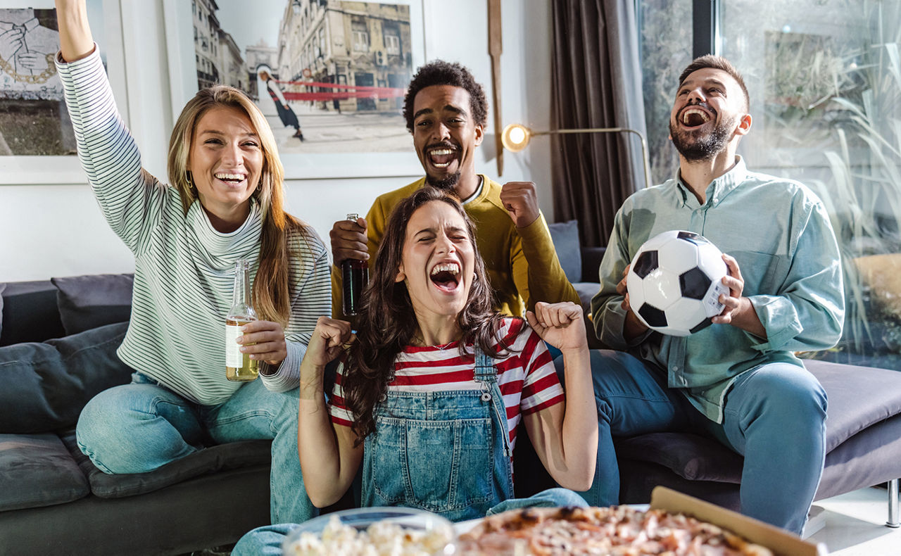 Mehrere Personen sitzen zusammen auf einem Sofa und jubeln