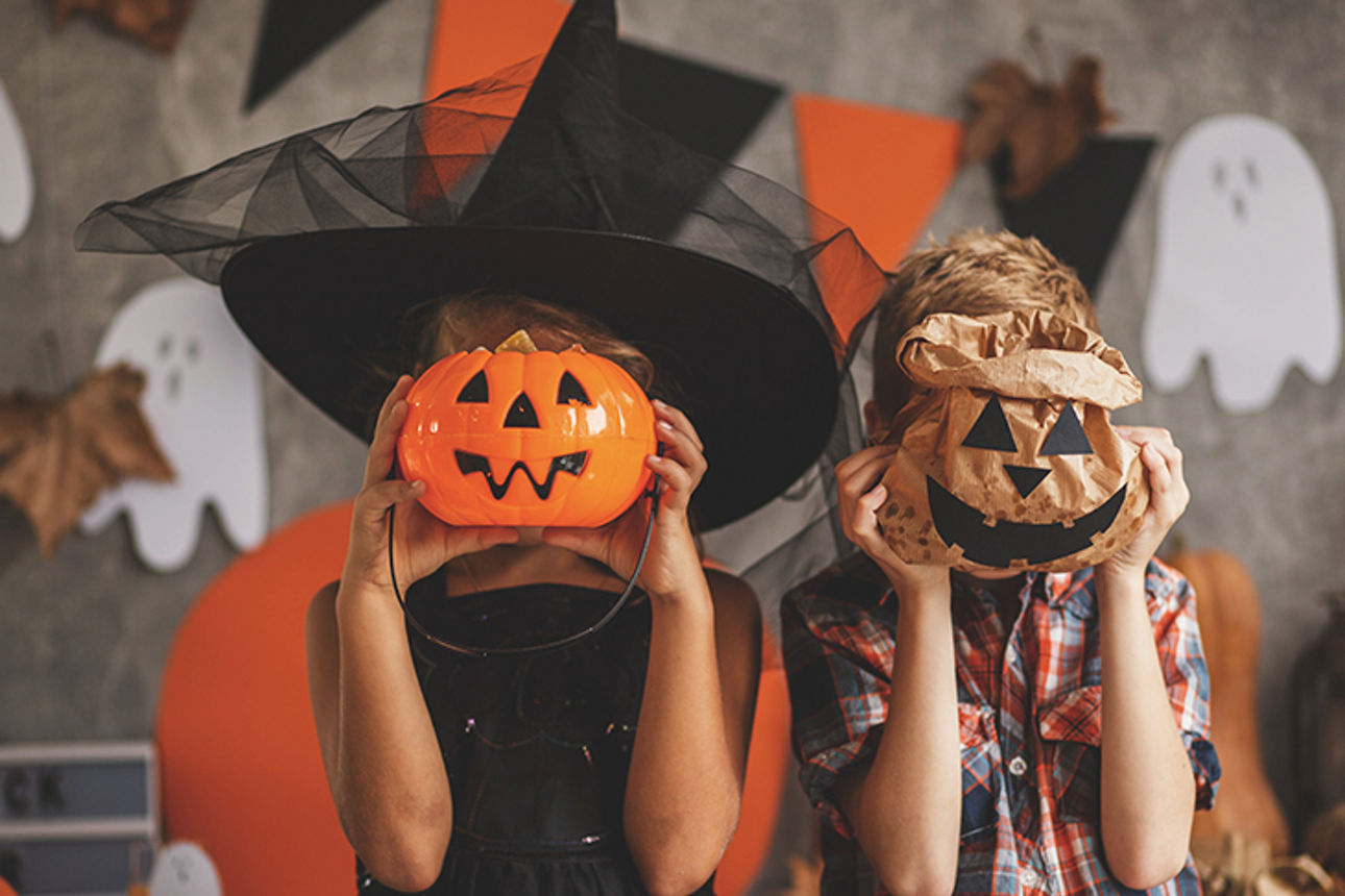 Kinder in Halloween-Kostümen mit Deko-Kürbissen in den Händen