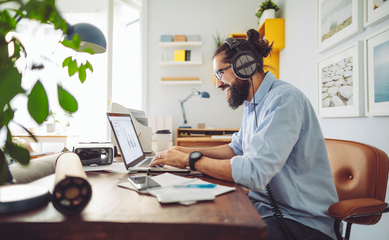 Mann sitzt mit Laptop und Kopfhörern im Homeoffice
