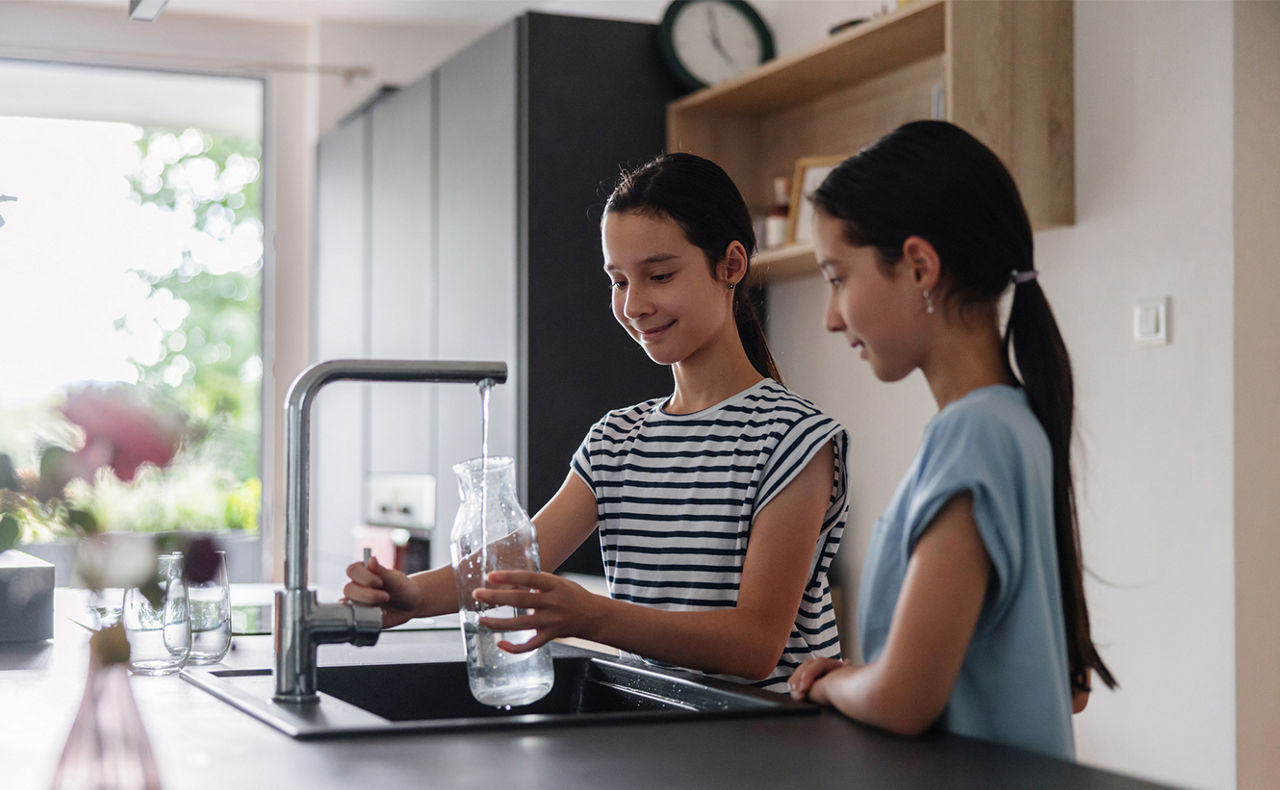 Zwei Kinder füllen eine Flasche am Wasserhahn in der Küche