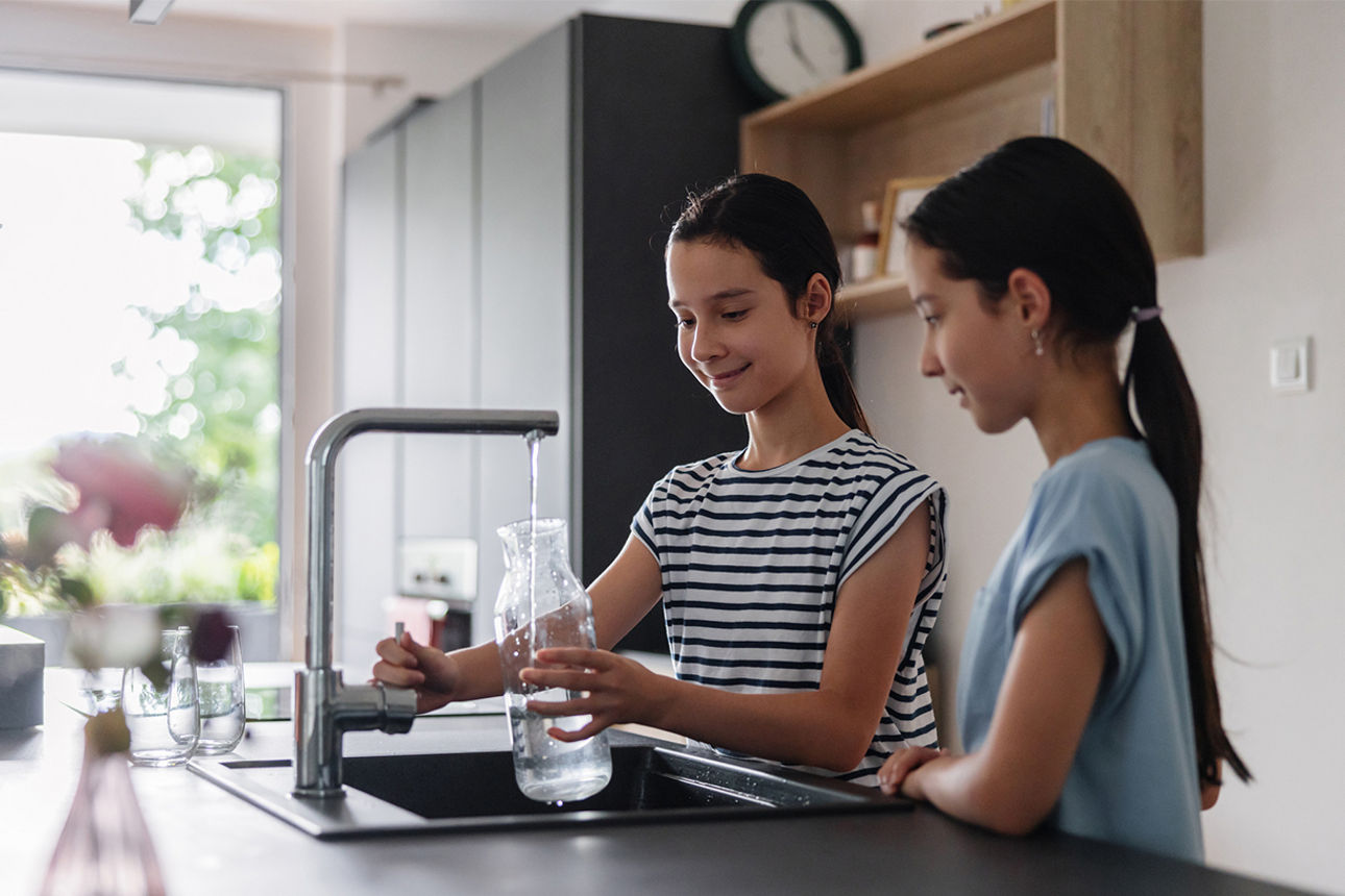Zwei Kinder füllen eine Flasche am Wasserhahn in der Küche