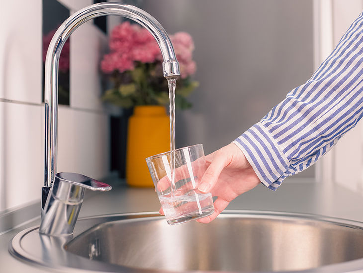 Person hält Glas unter einen Wasserhahn in der Küche