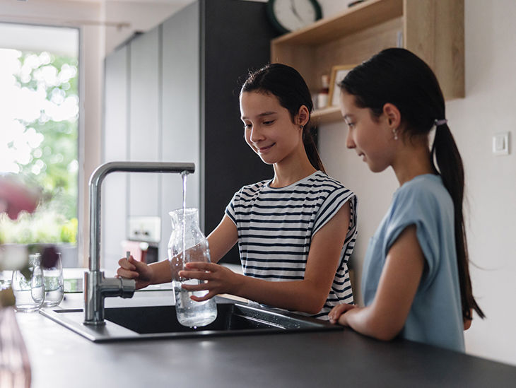 Zwei Kinder füllen eine Flasche am Wasserhahn in der Küche