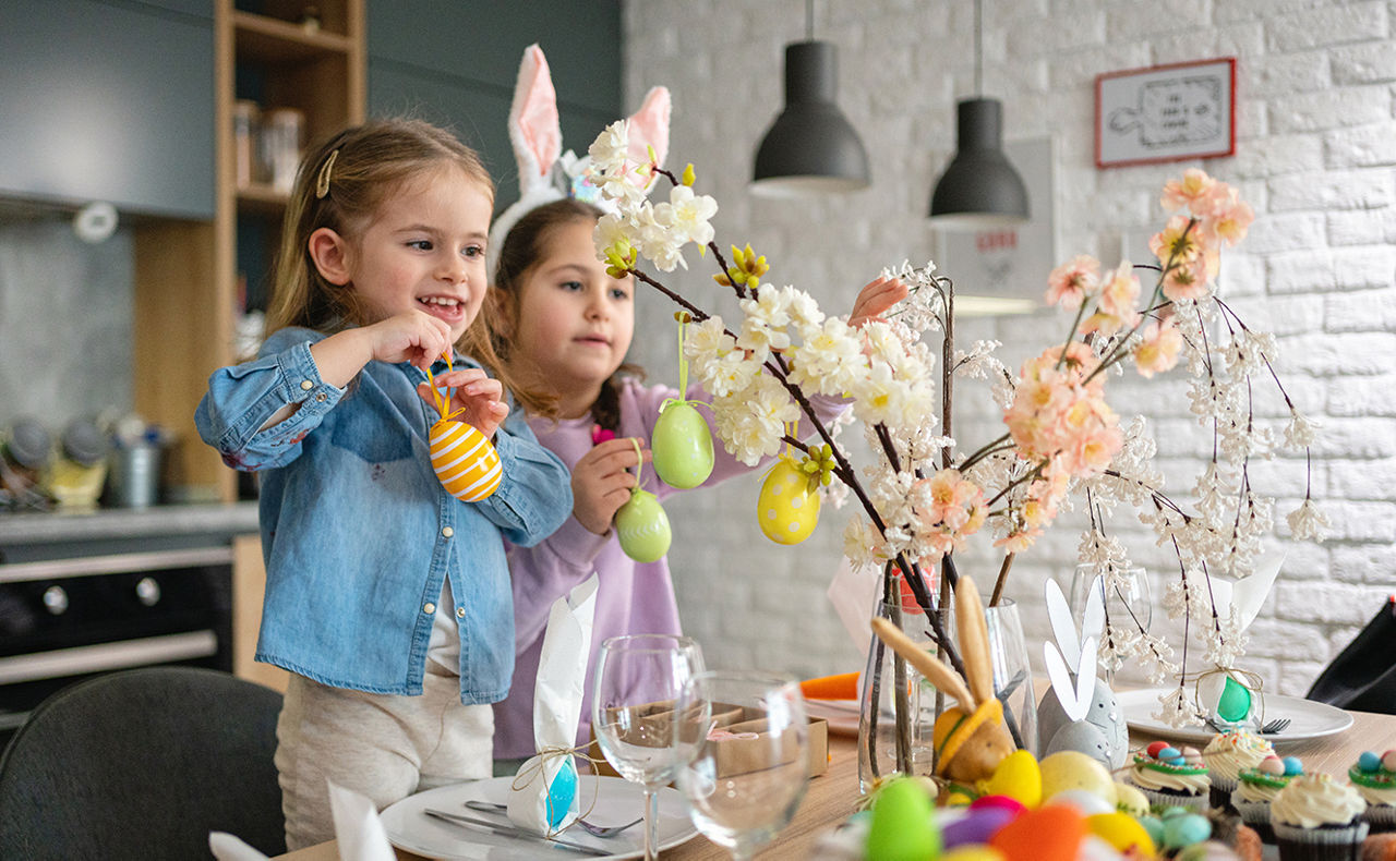 Zwei Kinder hängen Ostereier an einen Zweig