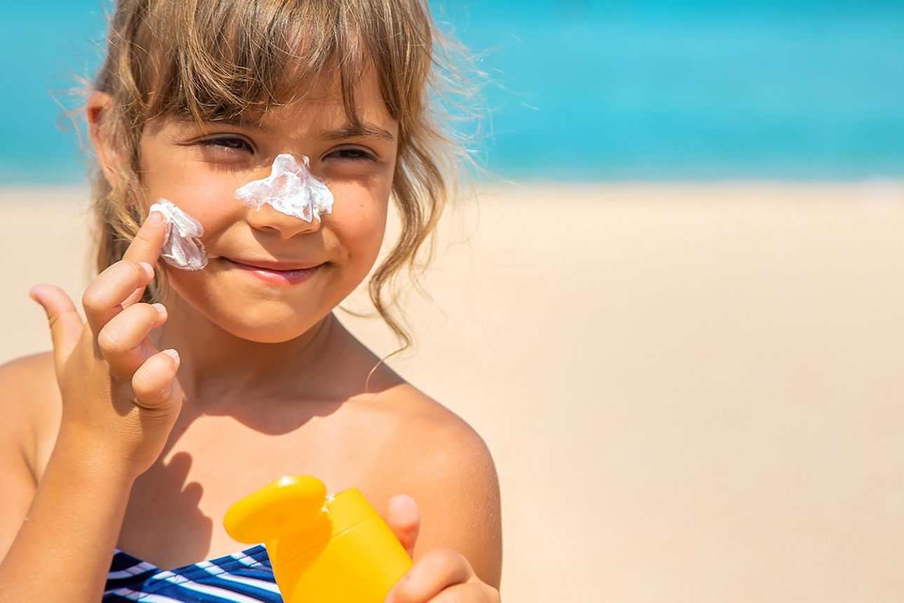 Kind am Strand streicht sich Sonnencreme ins Gesicht