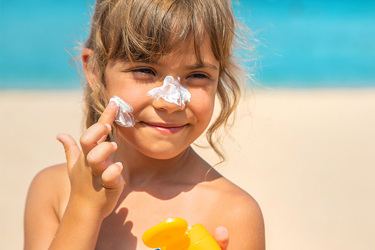 Kind am Strand streicht sich Sonnencreme ins Gesicht