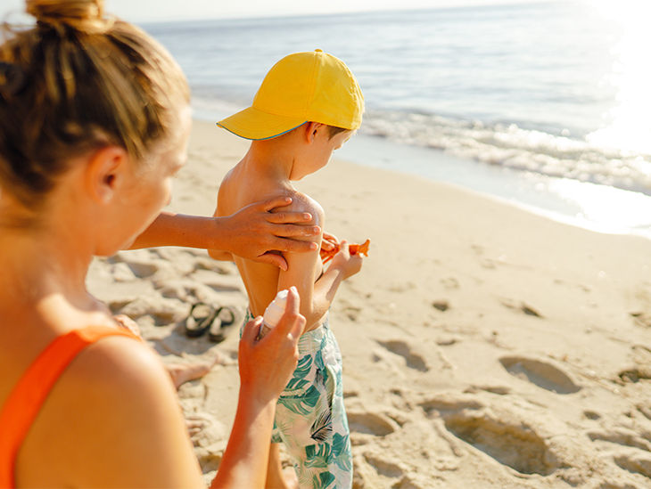 Mutter cremt Sohn am Strand ein – Sonnenschutz für die Haut