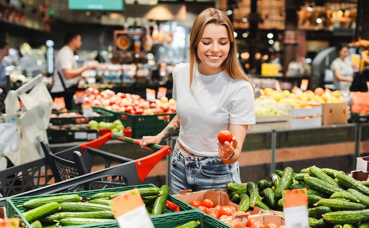 Frau steht im Supermarkt vor dem Gemüse-Regal