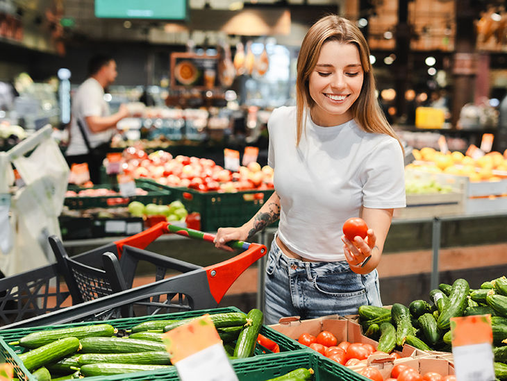 Frau im Supermarkt am Gemüsestand hält eine Tomate in der Hand