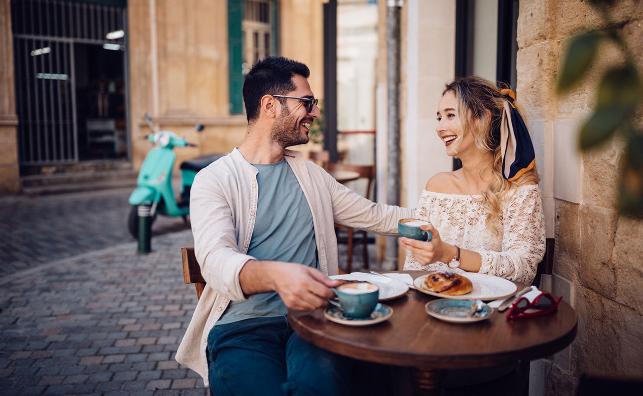 Mann und Frau sitzen draußen an einem Tisch und trinken Kaffee