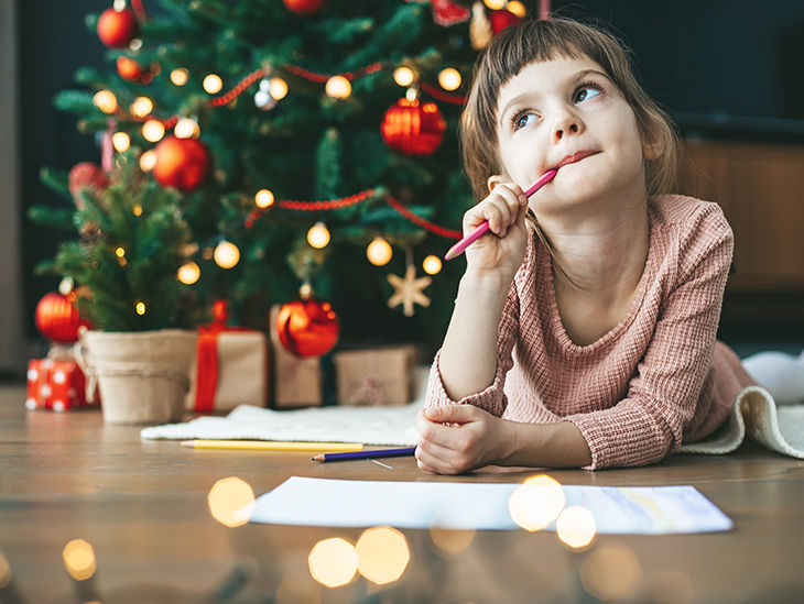 Kind liegt vor einem Weinachtsbaum mit Zettel und Stift