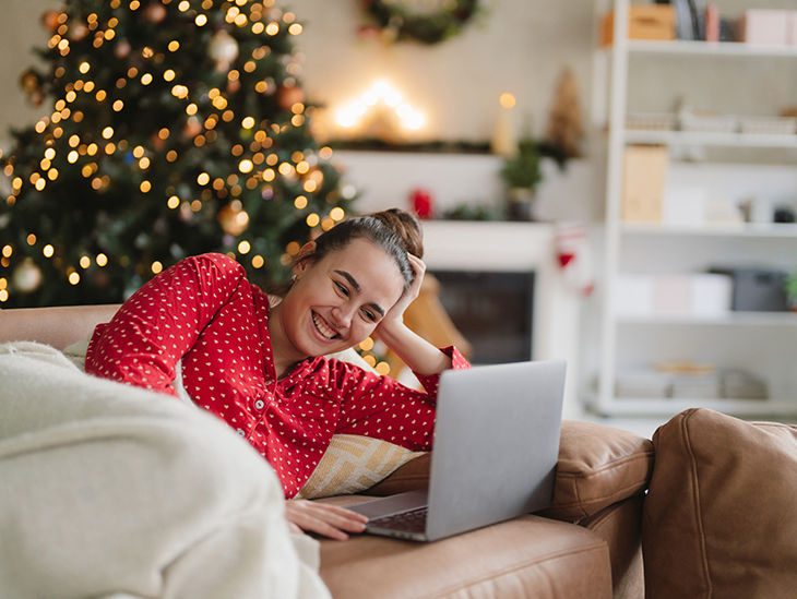 Frau mit Laptop liegt auf einem Sofa
