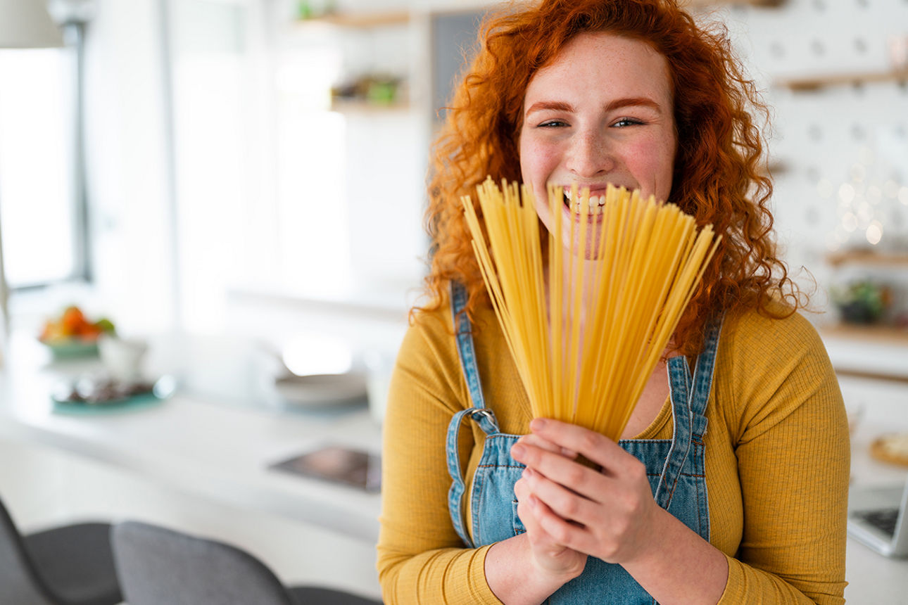 Frau hält Spaghetti wie einen Strauß vor ihr Gesicht