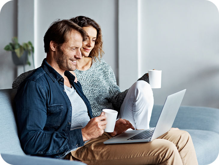 Paar sitzt auf einem Sofa und schaut auf einen Laptop