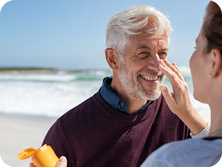 Frau cremt einen Mann am Strand das Gesicht ein