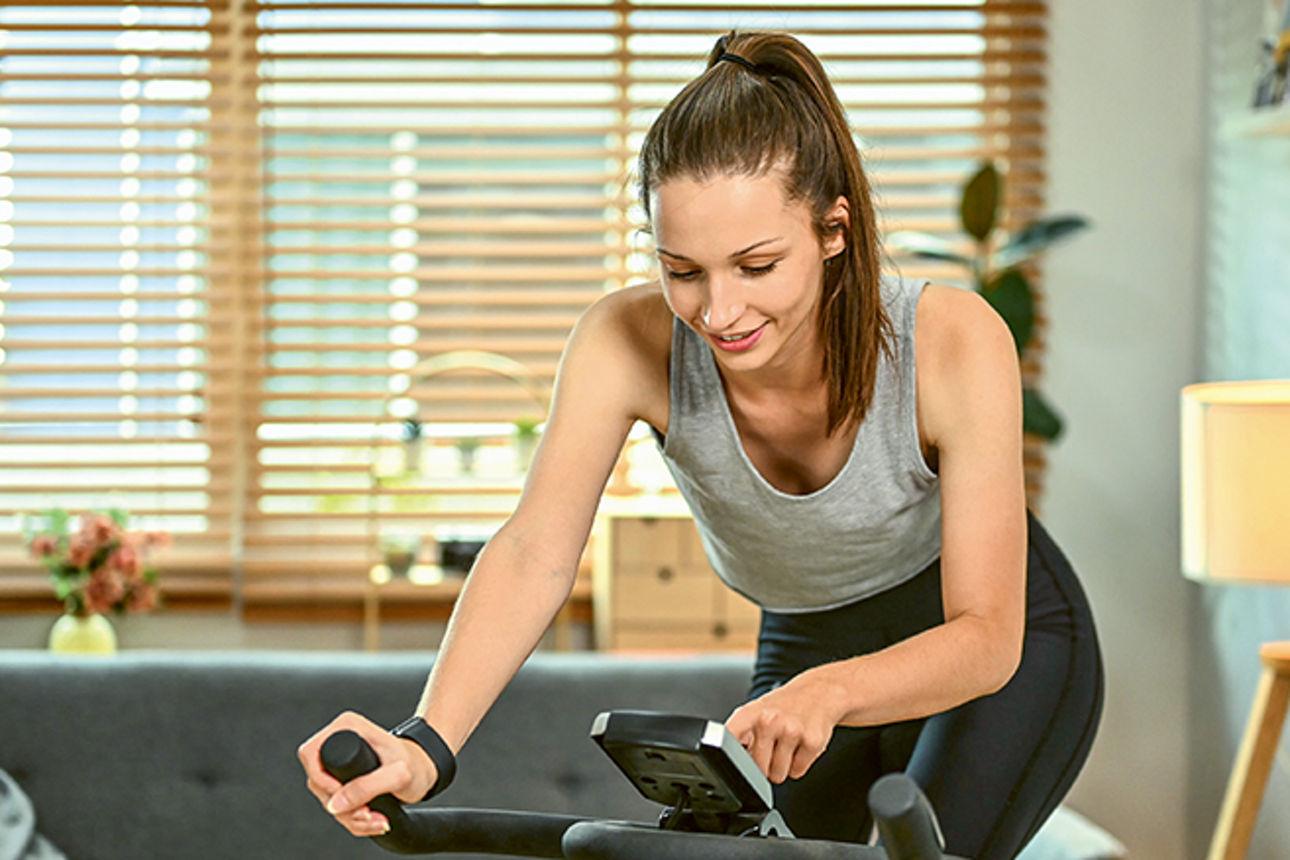 Junge Frau auf einem Ergometer in ihrem Wohnzimmer