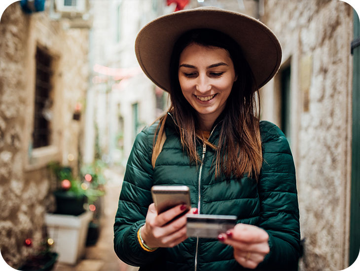 Frau schaut auf ihr Handy mit einer Bankkarte in der Hand