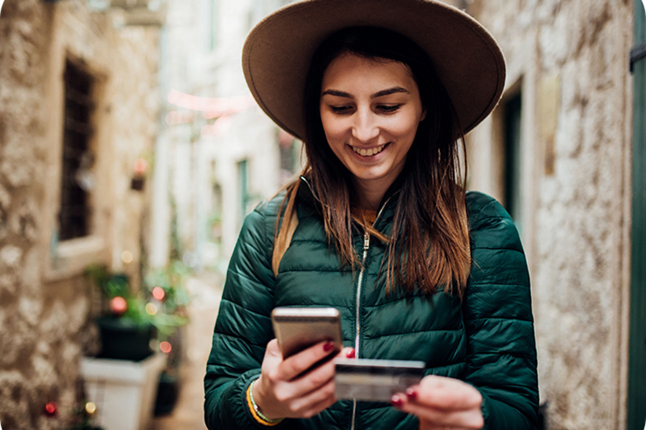 Frau schaut auf ihr Handy mit einer Bankkarte in der Hand