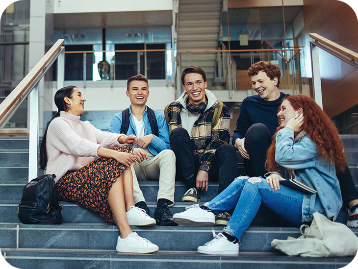 Fünf junge Menschen sitzen auf einer Treppe und lachen