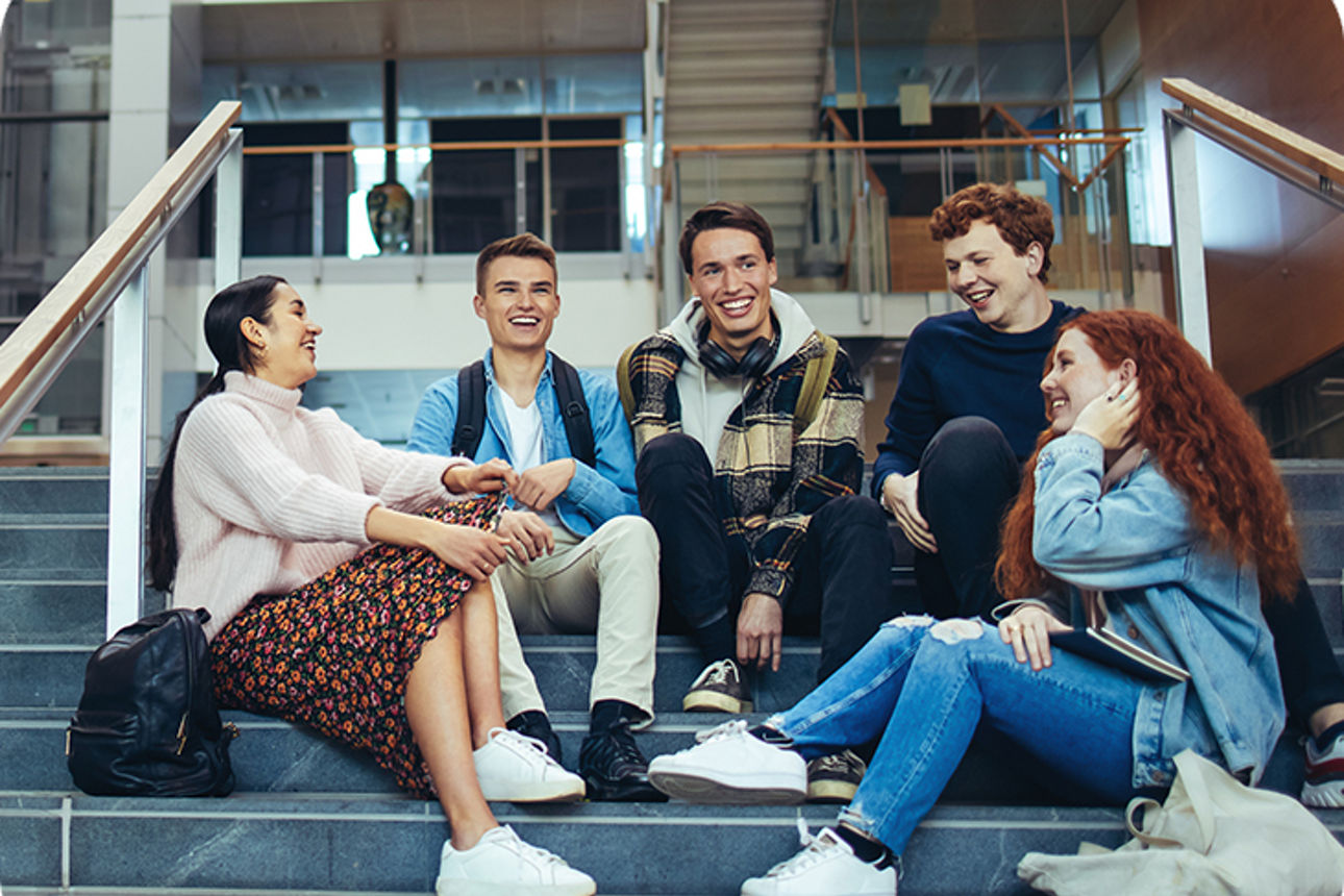 Fünf junge Menschen sitzen auf einer Treppe und lachen