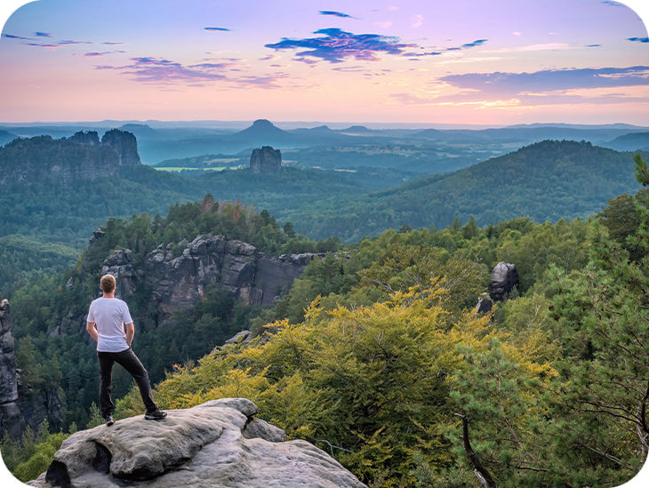 Mann steht auf einem Felsen vor einer Berglandschaft