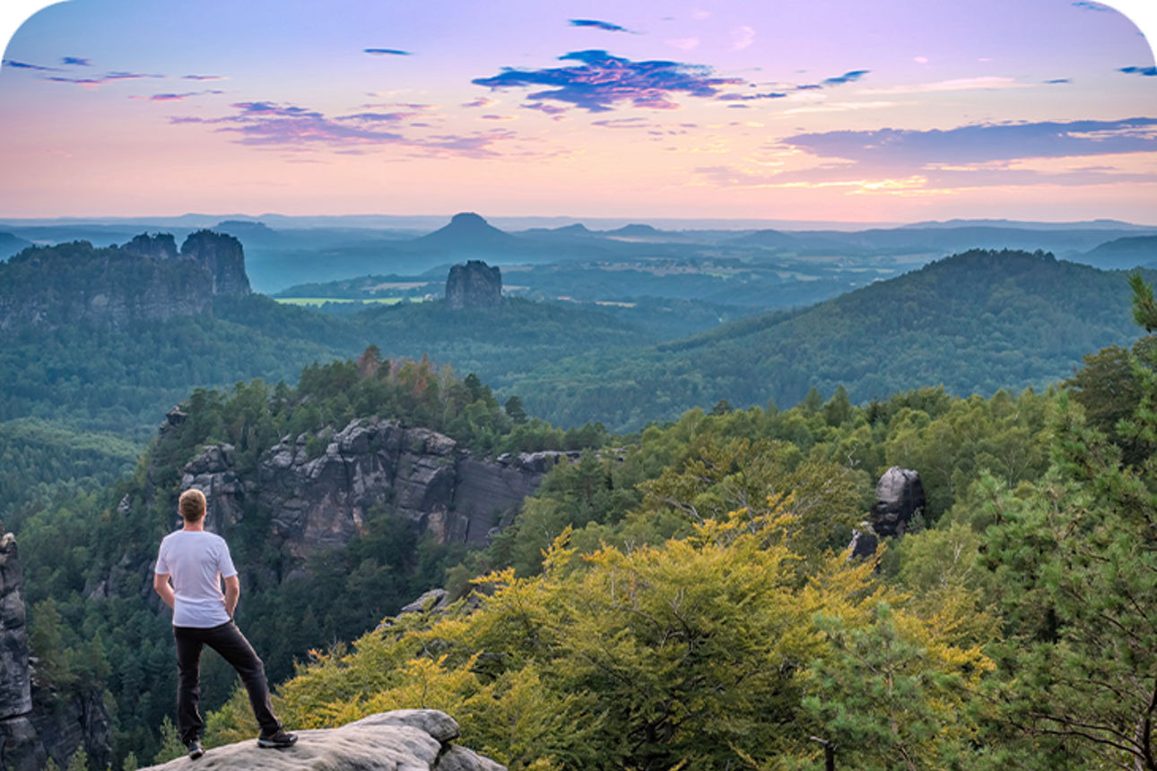 Mann steht auf einem Felsen vor einer Berglandschaft