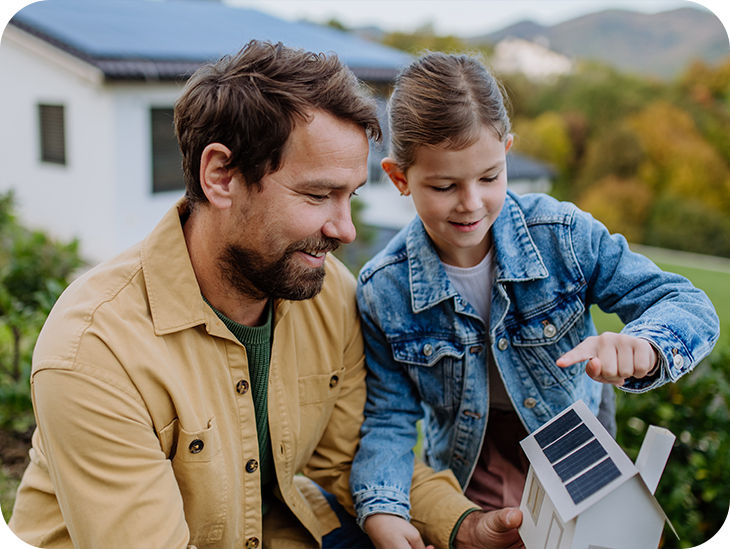 Mann hält mit seiner Tochter ein Miniatur-Haus mit Solarpanelen in der Hand