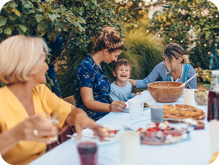 Mehrere Personen verschiedener Generationen sitzen im Garten an einem gedeckten Tisch