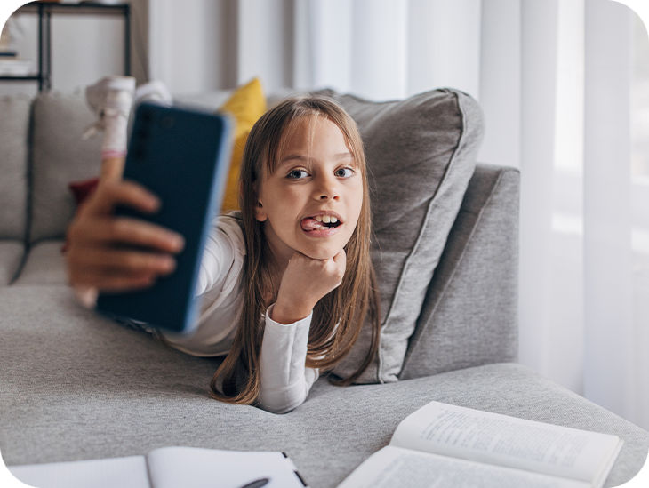Junges Mädchen liegt auf dem Sofa und macht ein Selfie