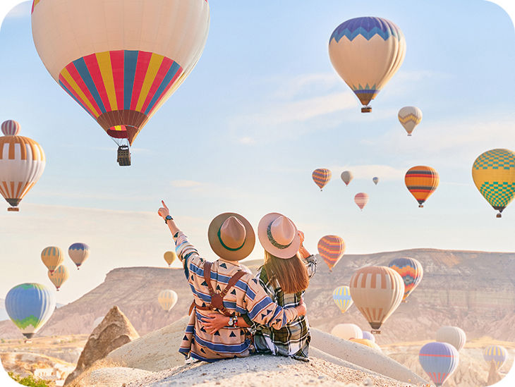 Ein Paar sitzt vor einer Landschaft mit vielen bunten Heißluftballons