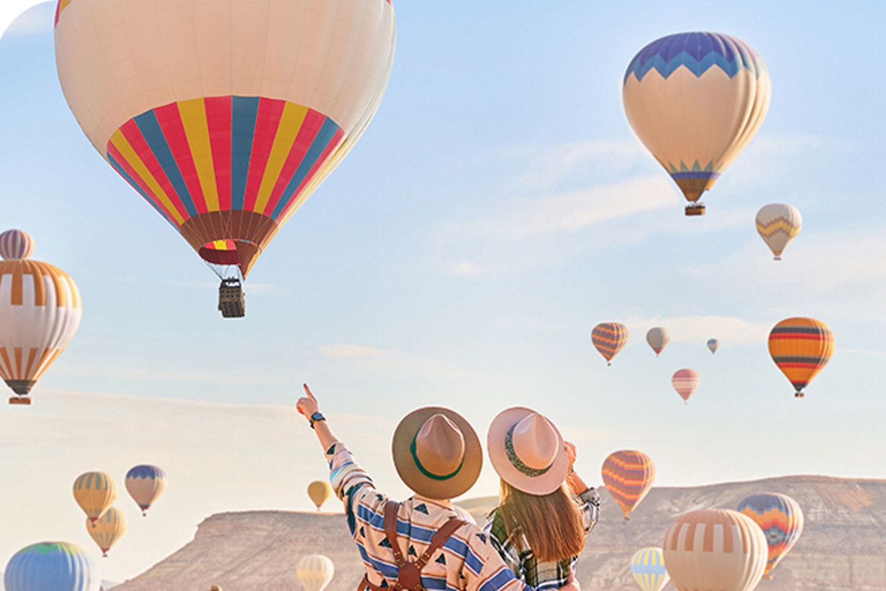 Ein Paar sitzt vor einer Landschaft mit vielen bunten Heißluftballons