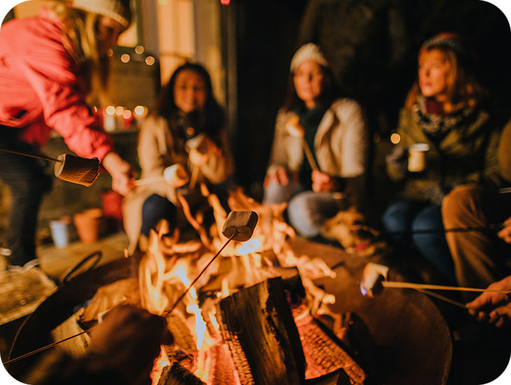 Viele Personen sitzen um eine Feuerschale und rösten Marshmallows